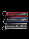 Three Addicted To Subi embroidered fabric key tags in red, blue and grey with classic Subaru car designs.